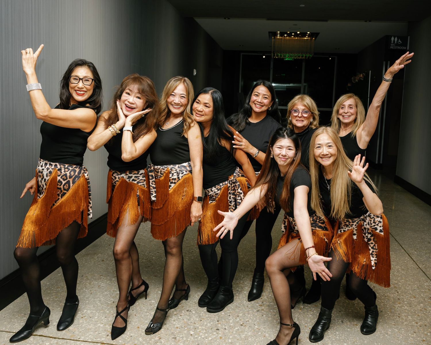 Energetic group photo of performers striking dynamic poses in a hallway.