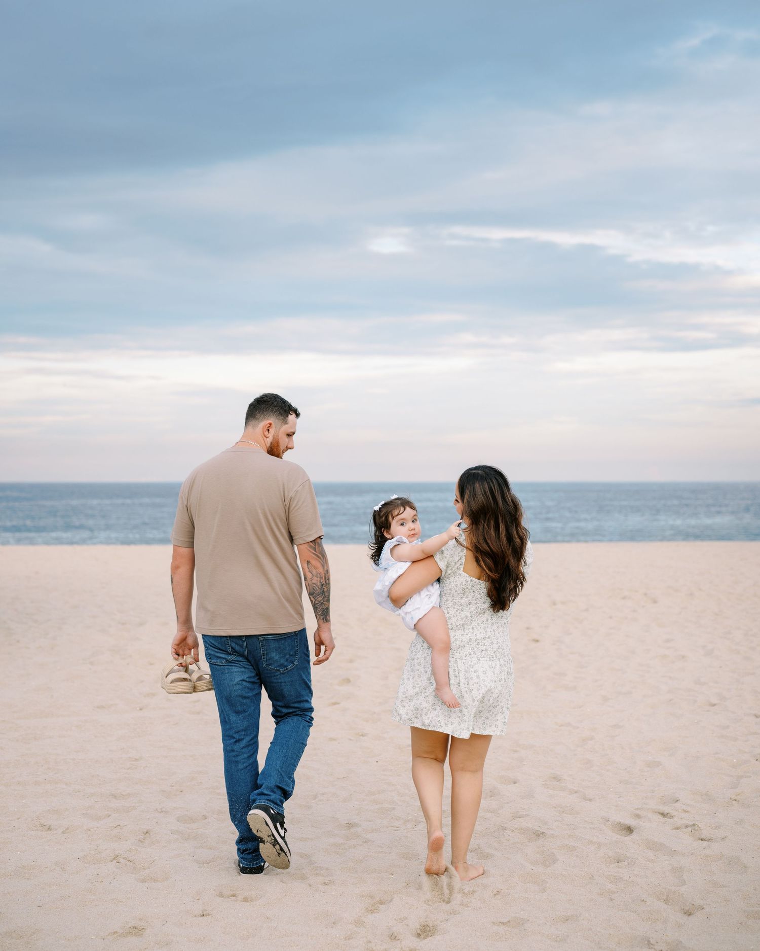 A couple walks hand in hand along a serene beach at sunset, leaving footprints in the sand.