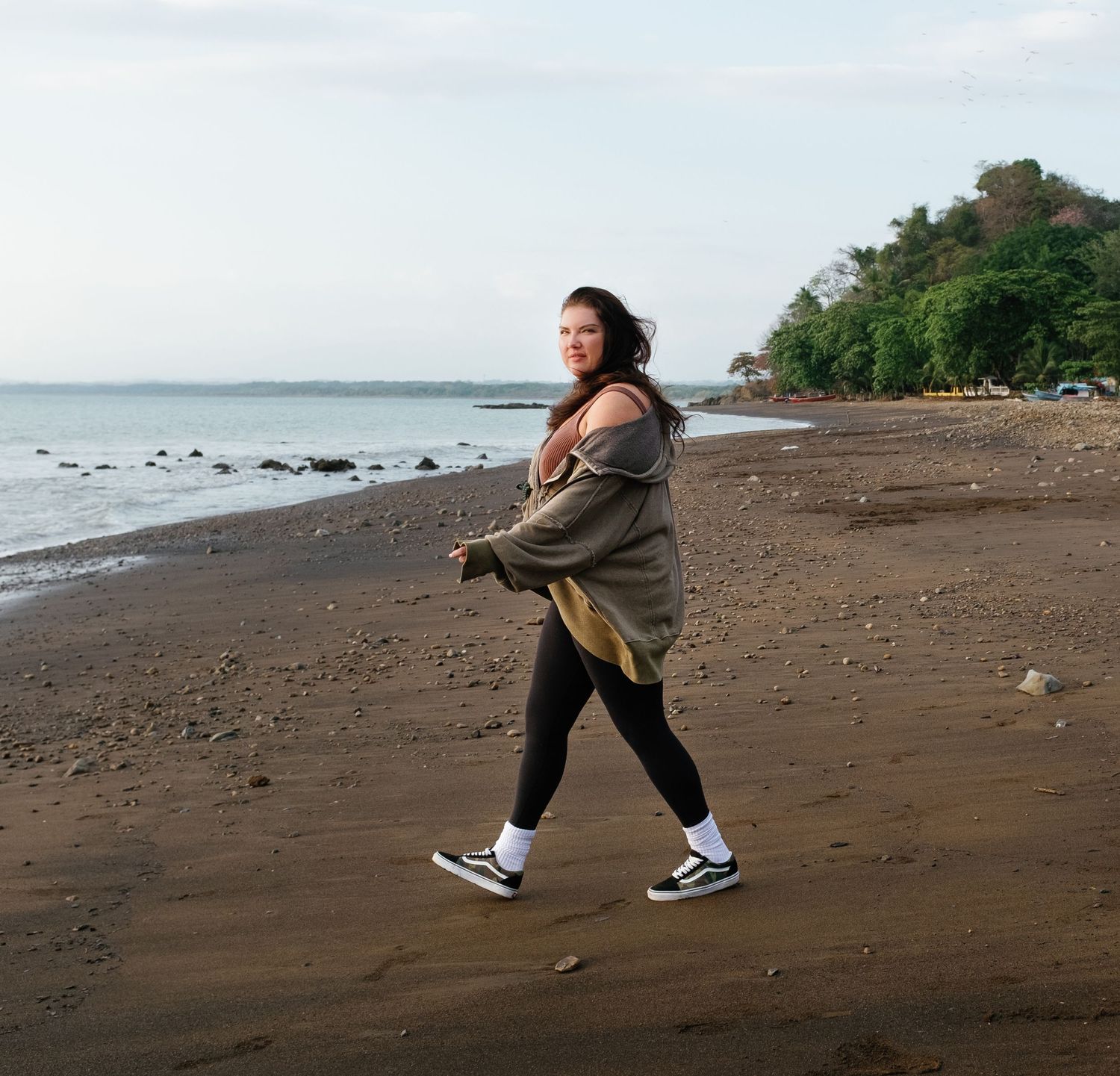 Person stretches and warms up on a dark sandy beach with ocean waves in the background.
