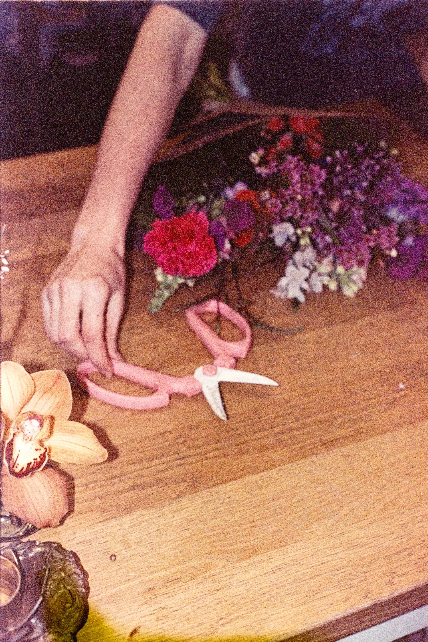Hands arranging colorful flowers and decorative elements on a light wooden surface in a floral design sequence.