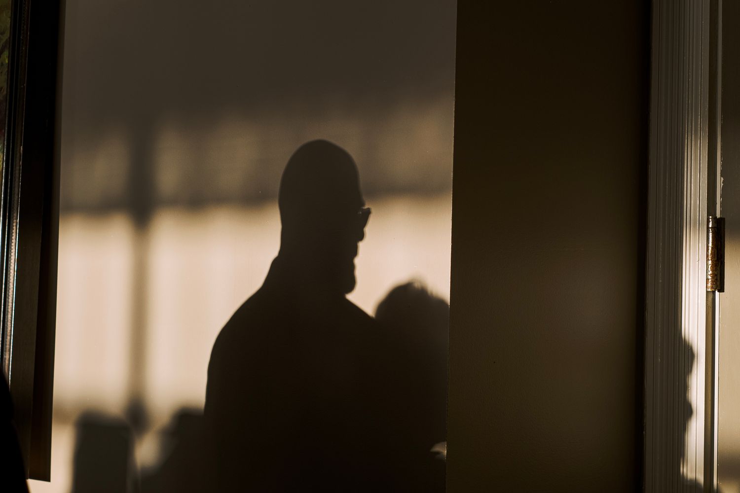 A dimly lit hallway with a dramatic silhouette of someone walking through a doorway at the end.