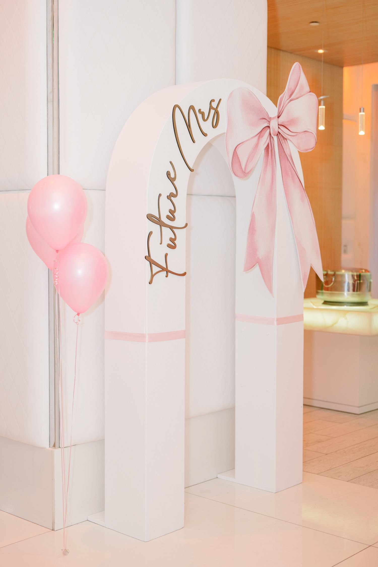 Pink heart-shaped balloons and bows decorating white pillars in an elegant event space interior.