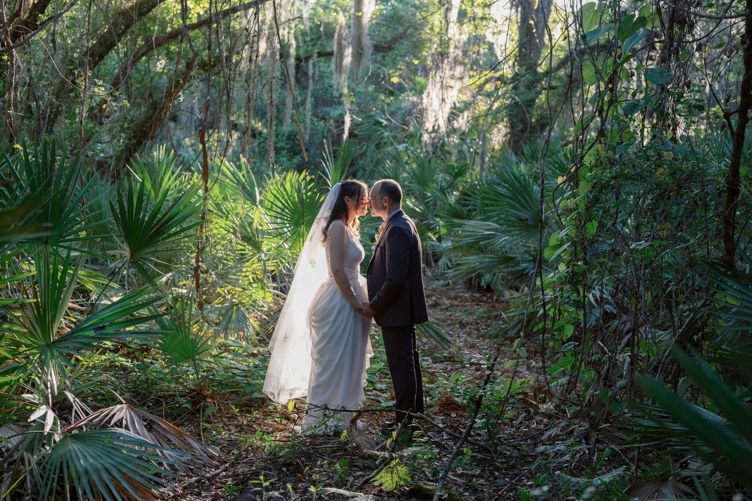 A couple walks through a lush tropical garden pathway surrounded by palm fronds and natural greenery.