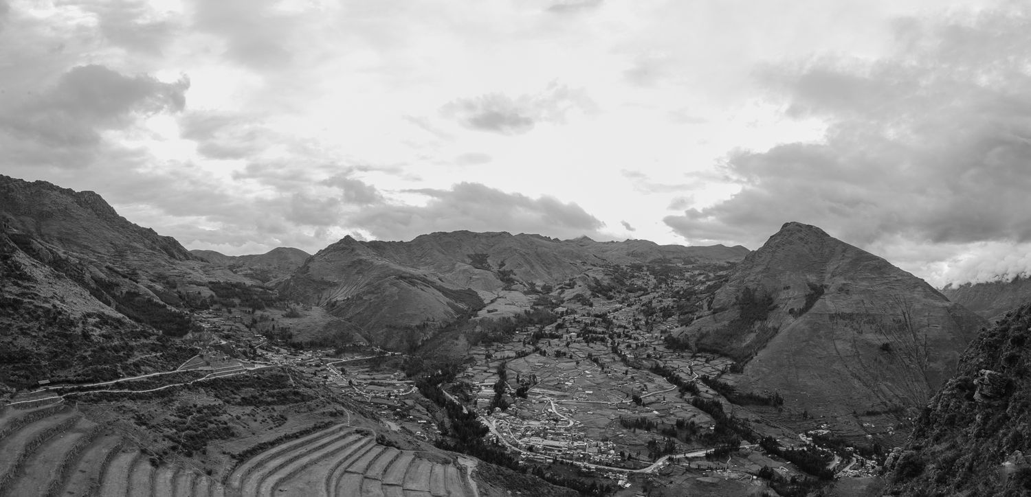 A panoramic view of rugged mountain peaks and valleys under dramatic cloudy skies in black and white.