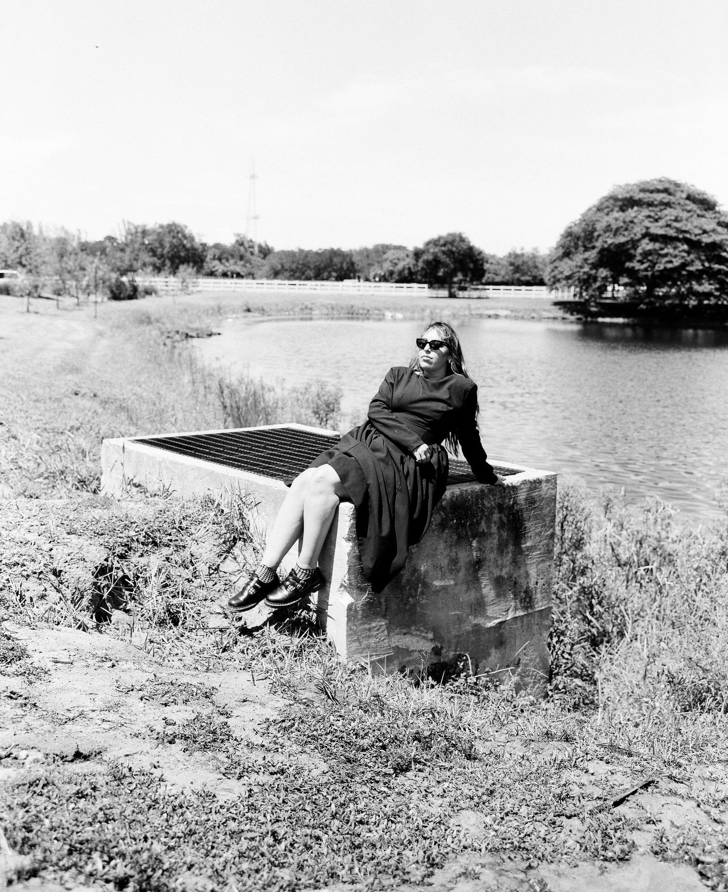 A person lying on a grassy hill by a lake reading a book in a black and white vintage photograph.