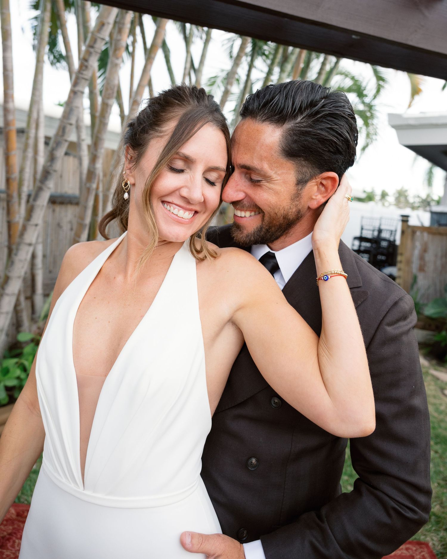 A couple shares a romantic moment outdoors, with the bride wearing a plunging white dress and groom in dark attire.