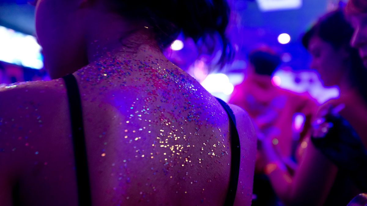 Woman with glitter on her back dancing in a nightclub under purple UV lights.