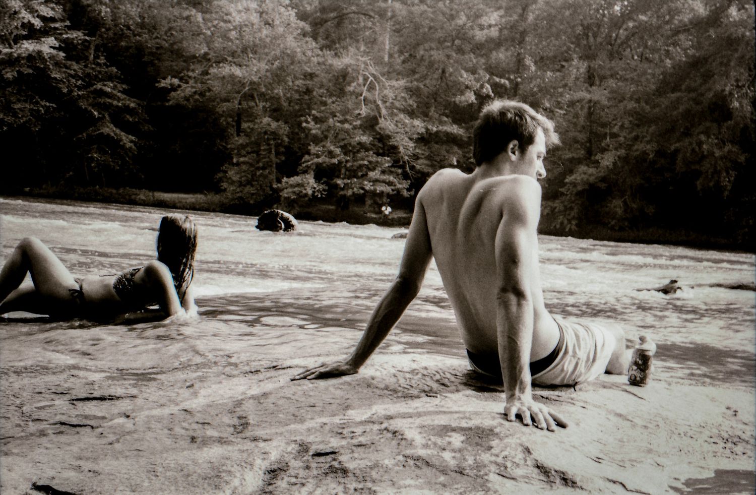 A series of black and white photographs showing a figure performing a rolling movement sequence on a sandy surface.