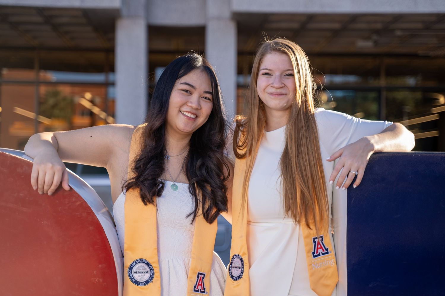 Nursing senior portrait of two grads with yellow stoles at the Bear Down sign on the University of Arizona campus, by N&D Media.