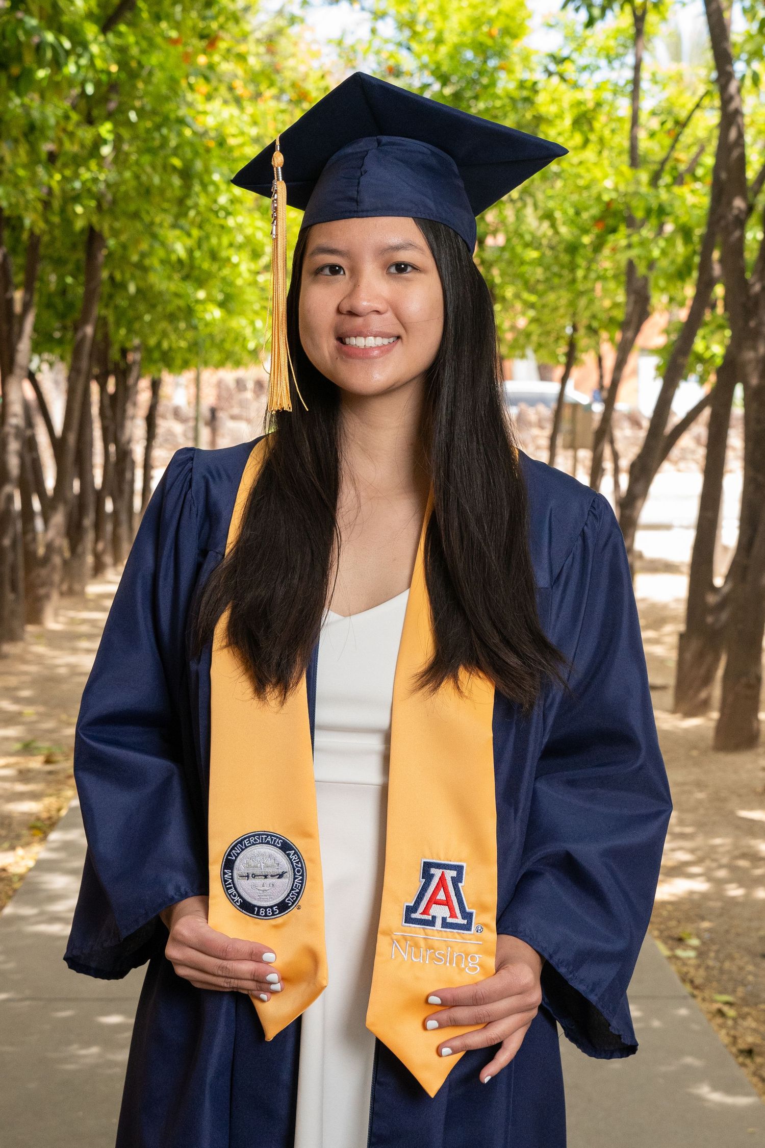 Nursing grad holding her stole on the Orange Grove pathway at the University of Arizona campus for senior portraits, by N&D Media.