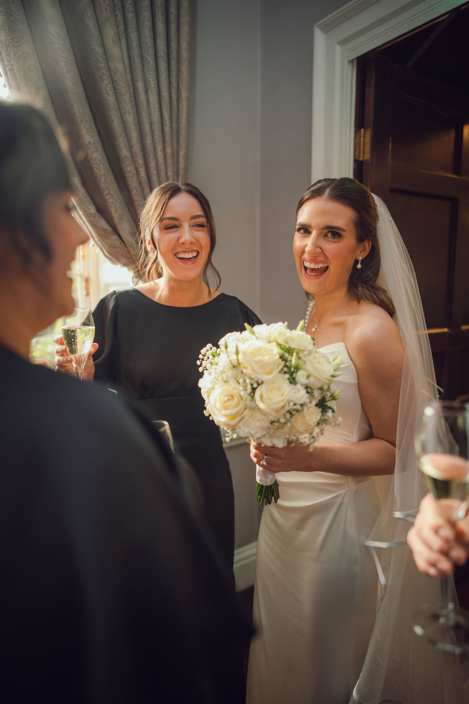 Bride in strapless gown laughs joyfully with bridesmaid in black dress at the Manor House Mount Juliet wedding Kilkenny.