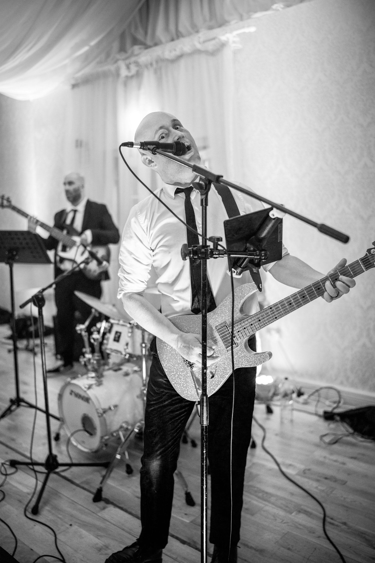 Black and white photo of a bald guitarist singing passionately on stage at a wedding reception.