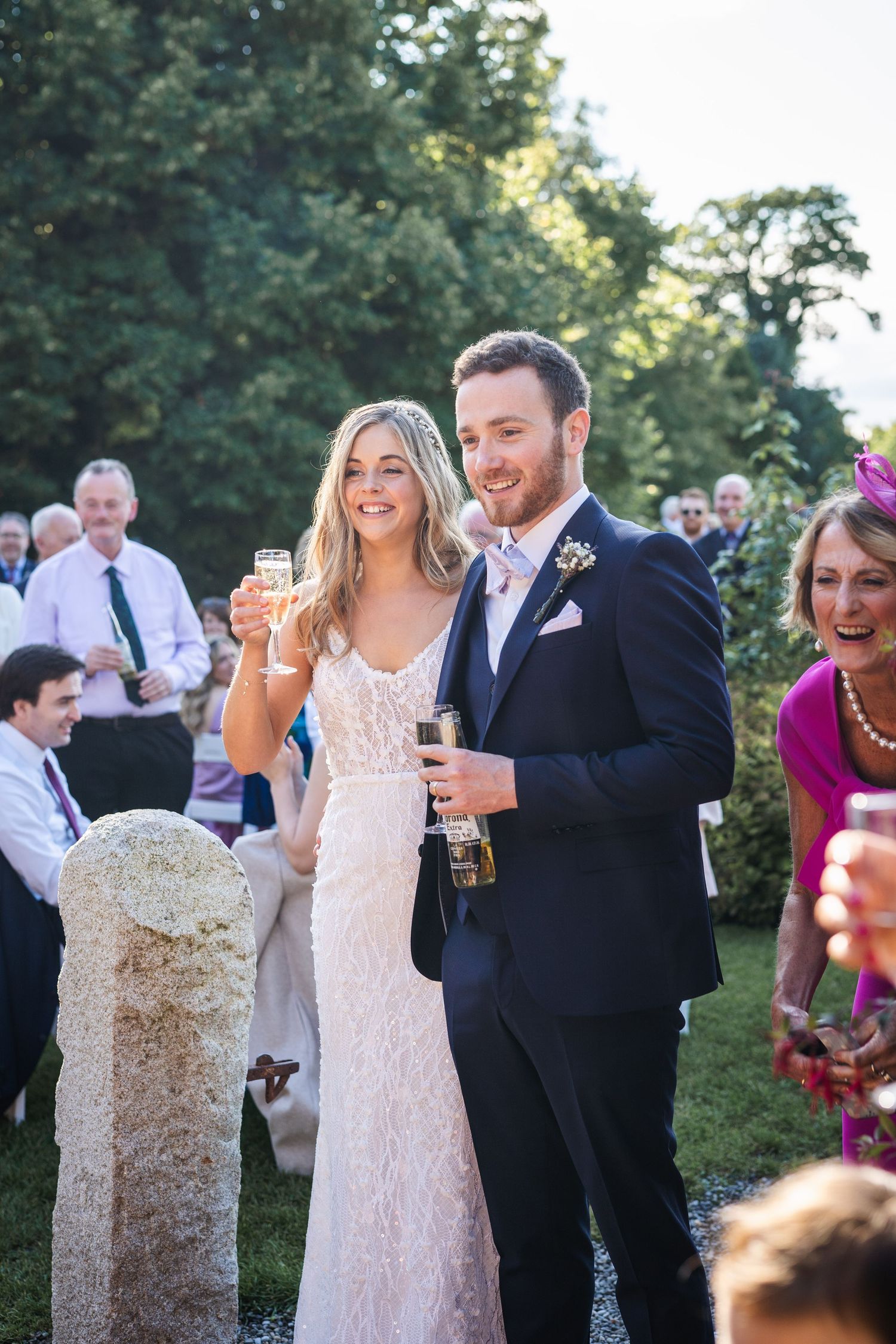 Smiling bride and groom toasting with champagne at outdoor wedding reception.