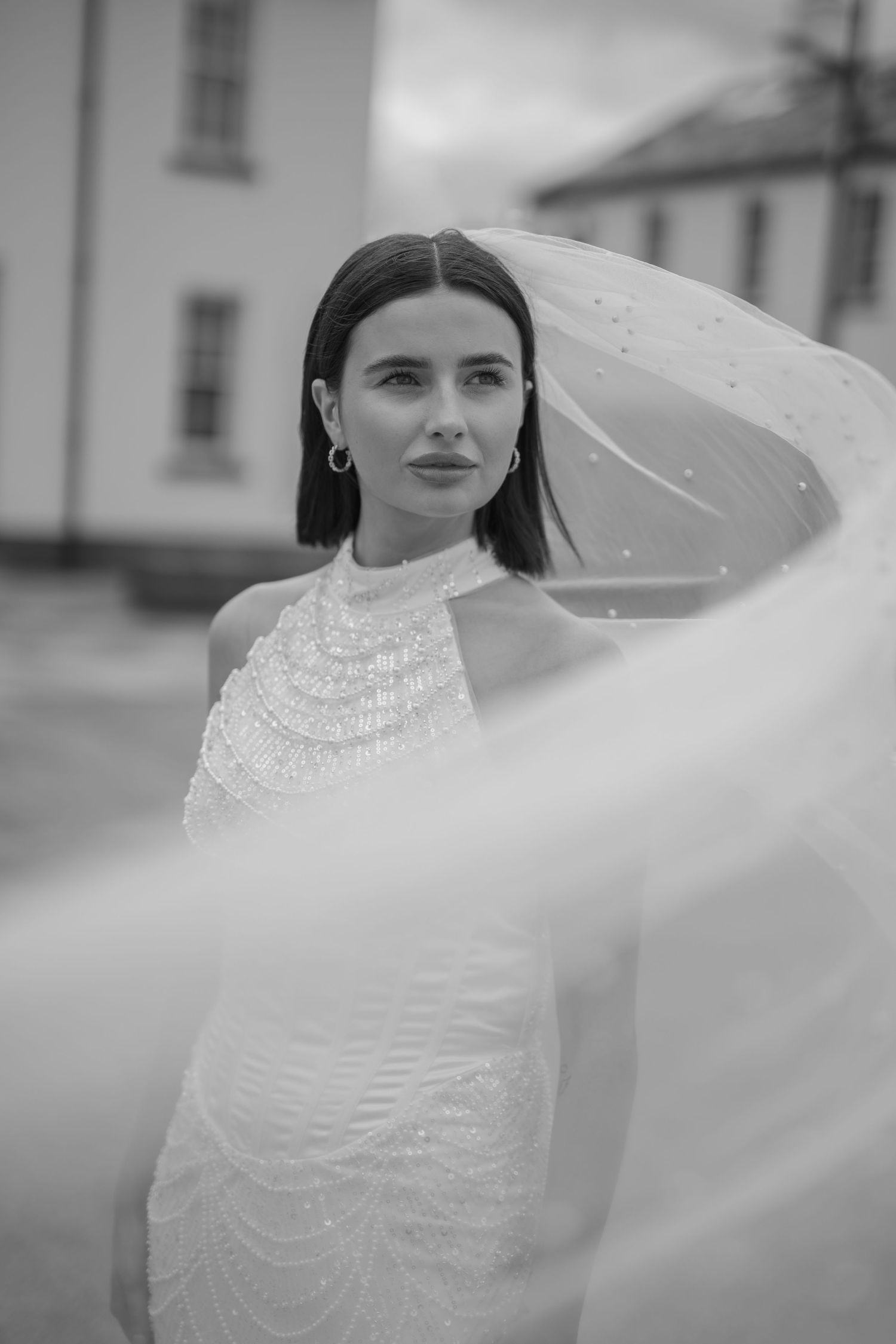 Elegant bride in beaded halter wedding gown with flowing veil, black and white portrait photography.