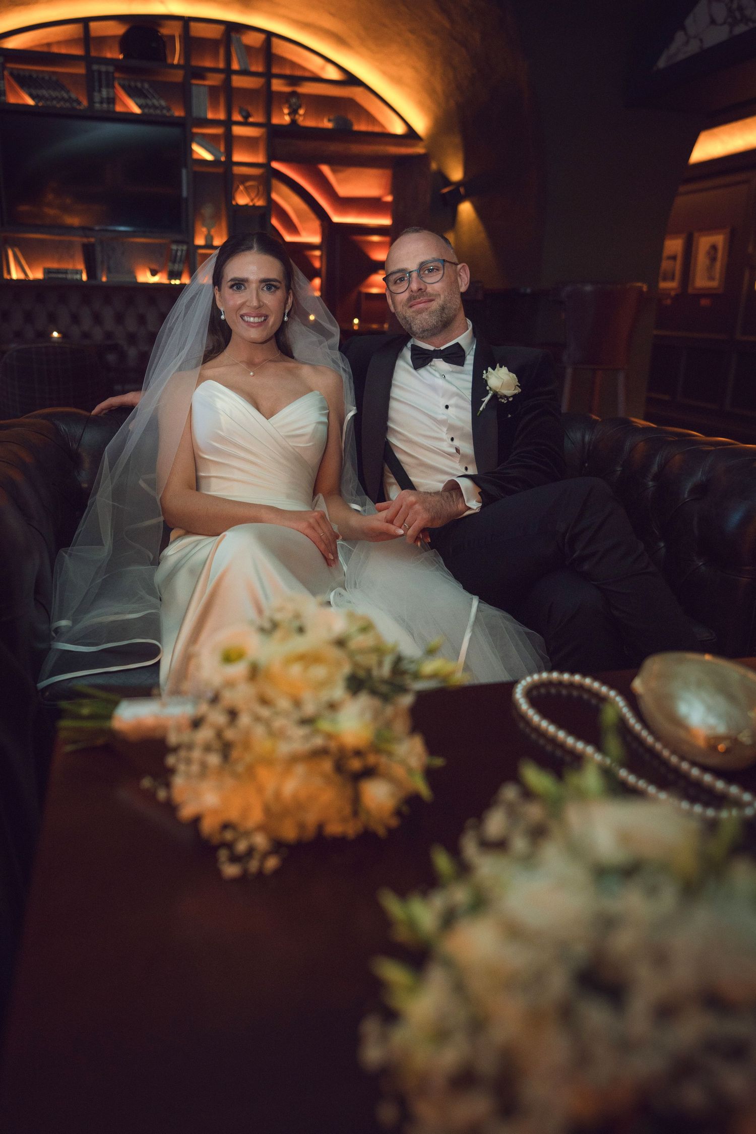 Smiling bride and groom relax on a leather sofa with bouquet at the Manor House Mount Juliet wedding Kilkenny.