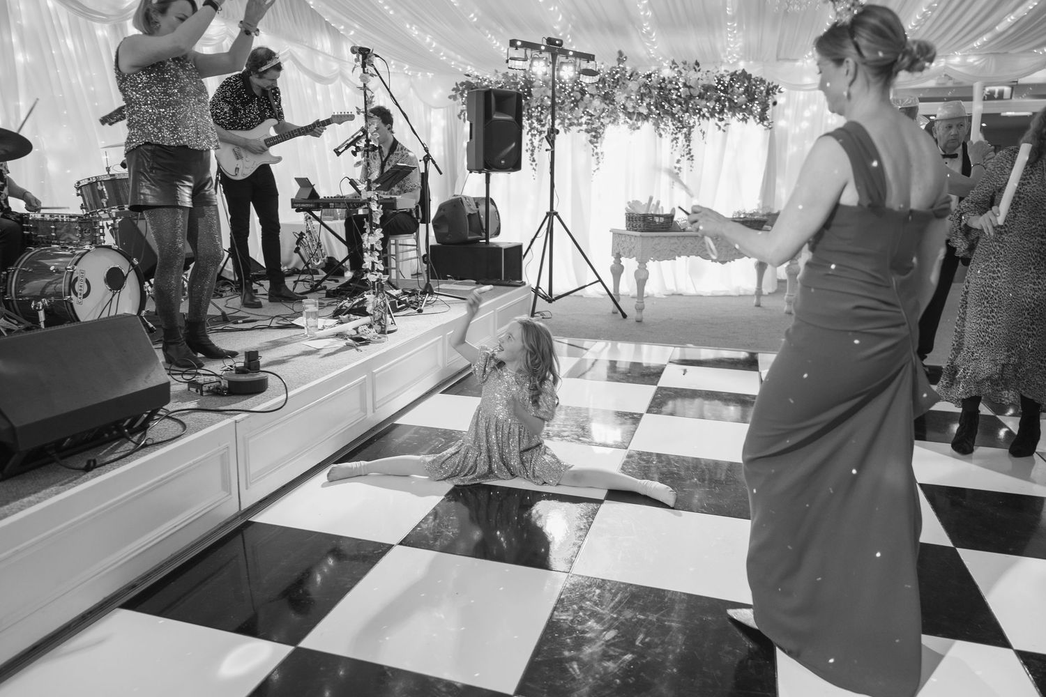 Guests dance on a checkered floor at a wedding reception with a live band performing on stage.
