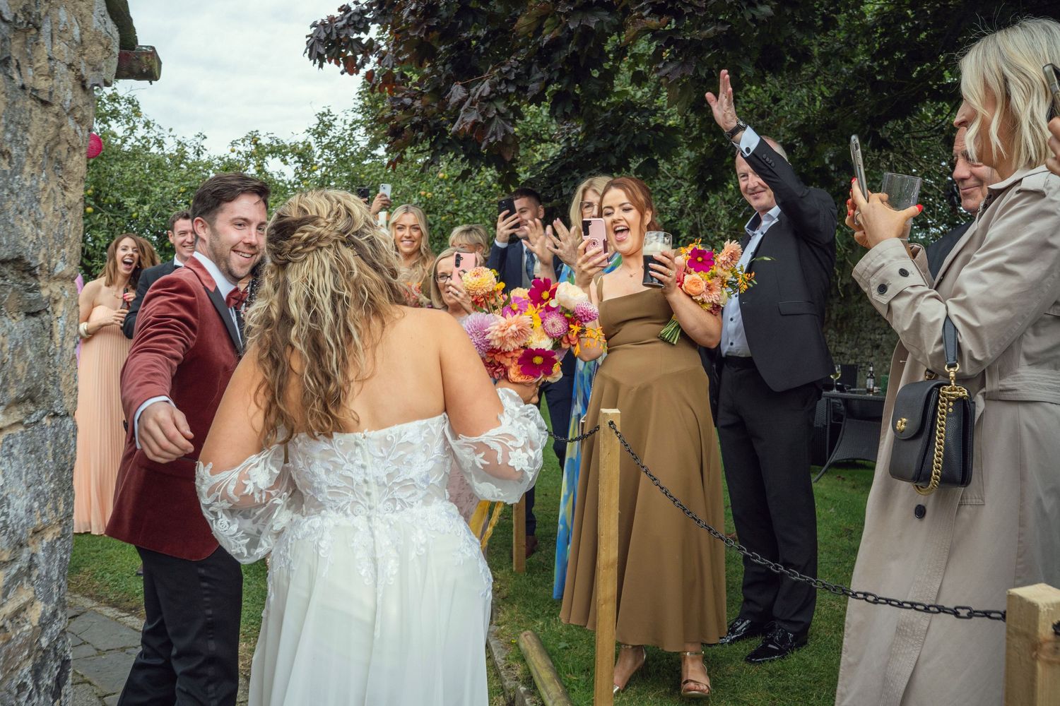 Joyful bride and groom greeted by celebrating wedding guests holding vibrant bouquets at outdoor garden wedding reception in Co Meath.