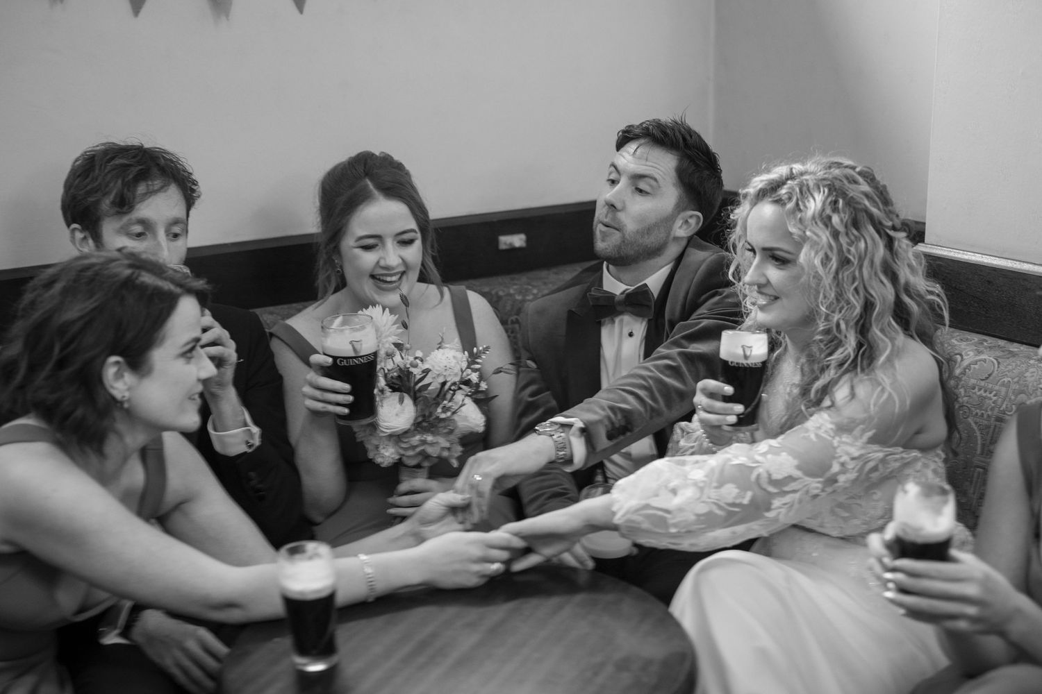 Black and white photo of bride and wedding guests laughing and holding hands at reception table outdoor garden wedding reception in Co Meath