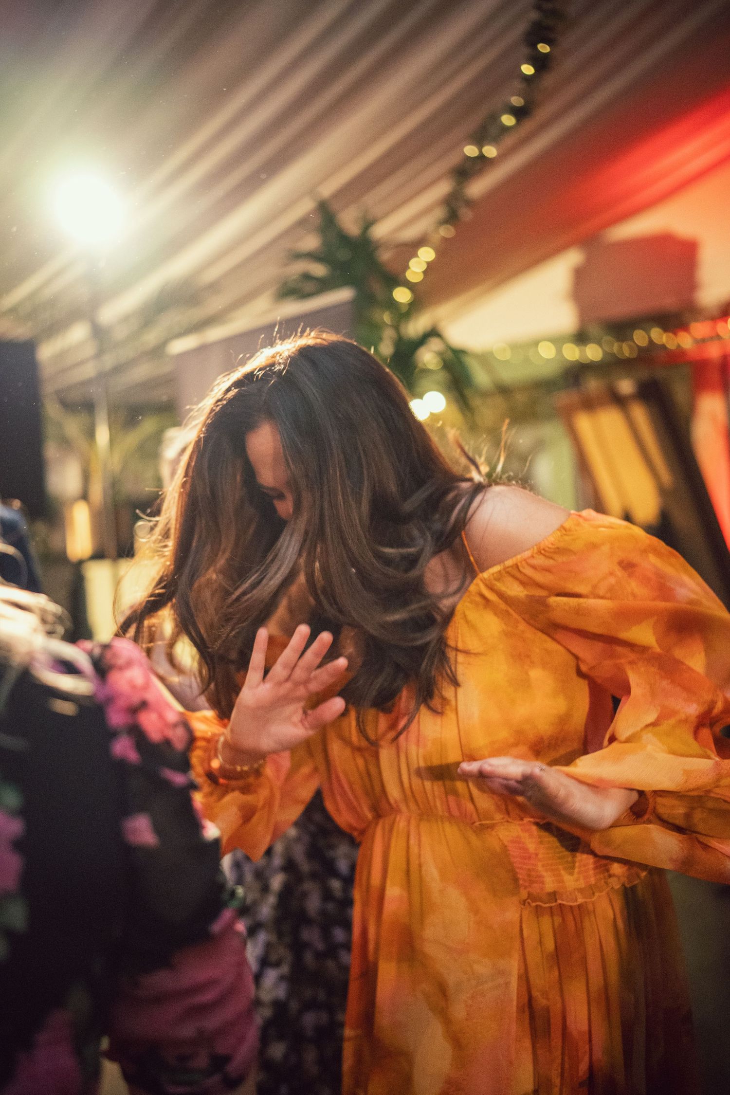 Woman in flowing orange dress dancing energetically under warm lights at a lively wedding reception party.