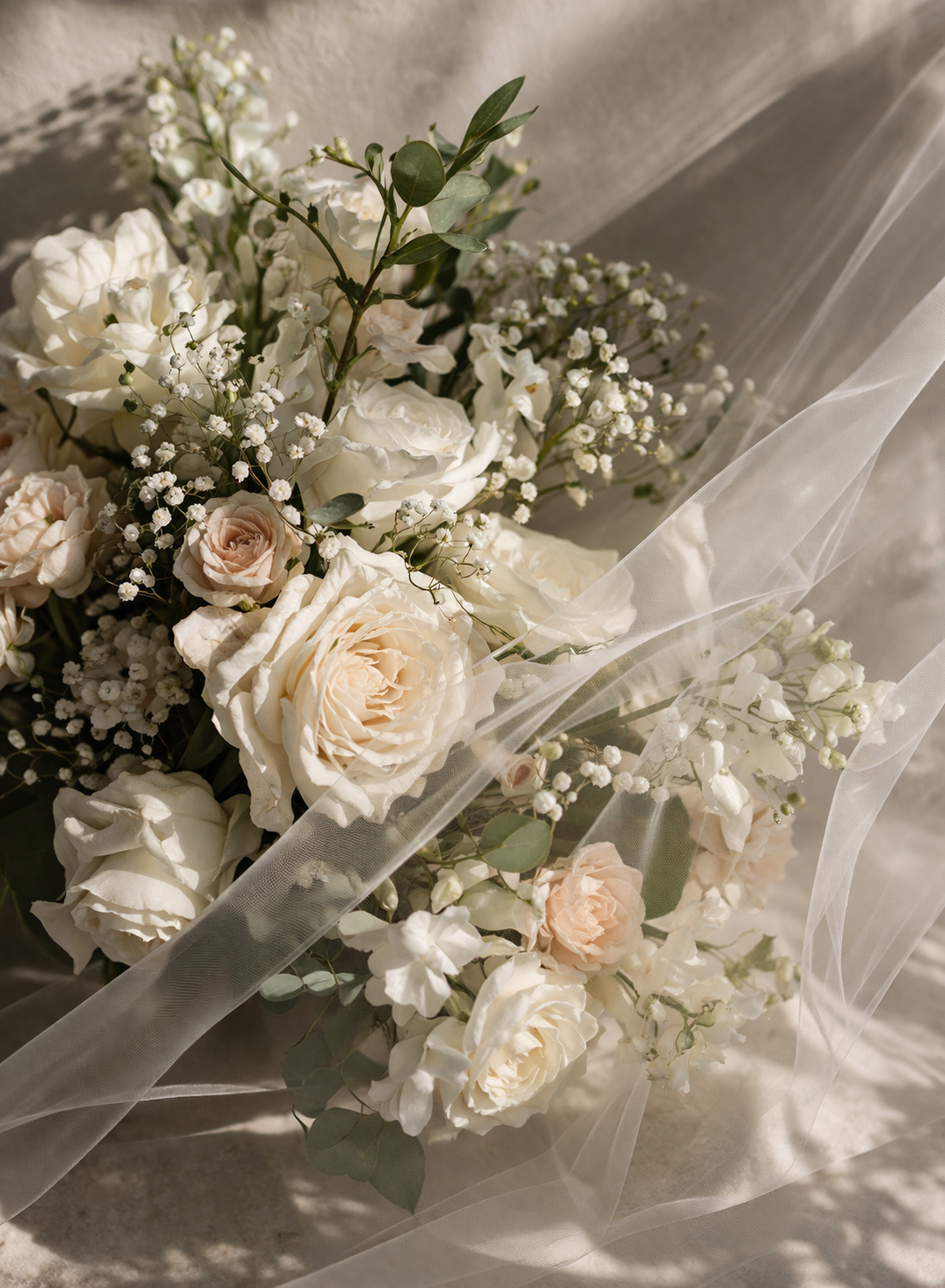 Elegant wedding bouquet of white and blush roses with baby's breath arranged on soft white tulle fabric.