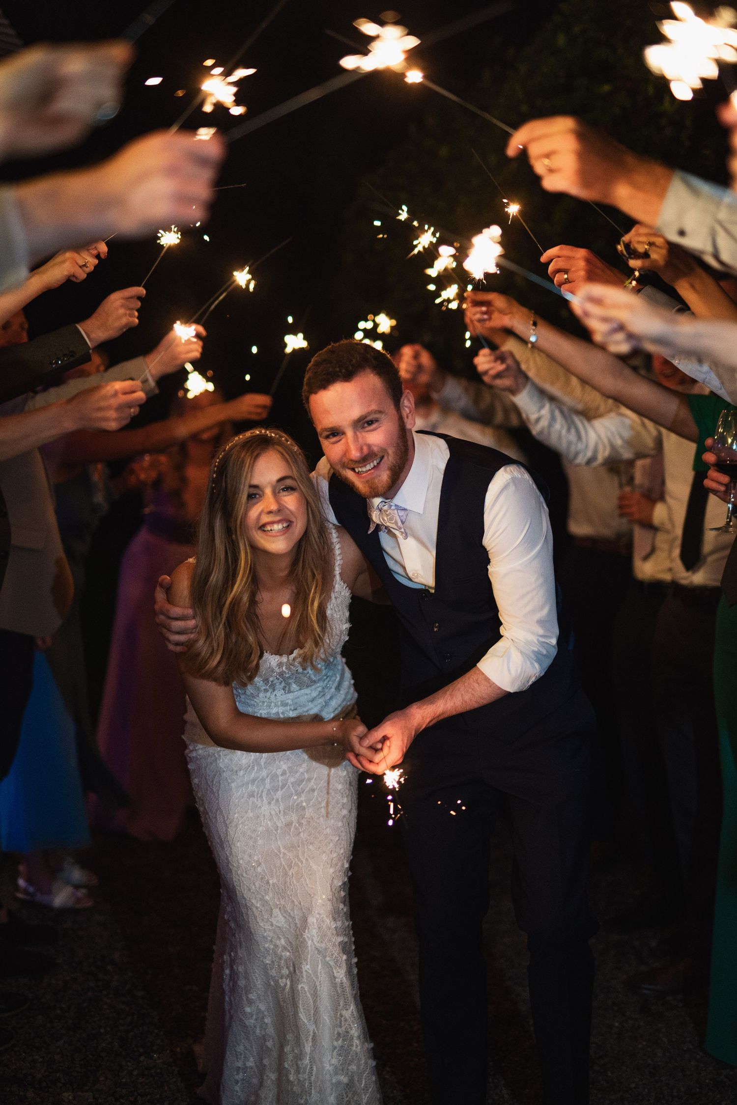 Bride and groom smile joyfully while walking through a tunnel of sparklers at Rathsallagh House wedding in Wicklow.