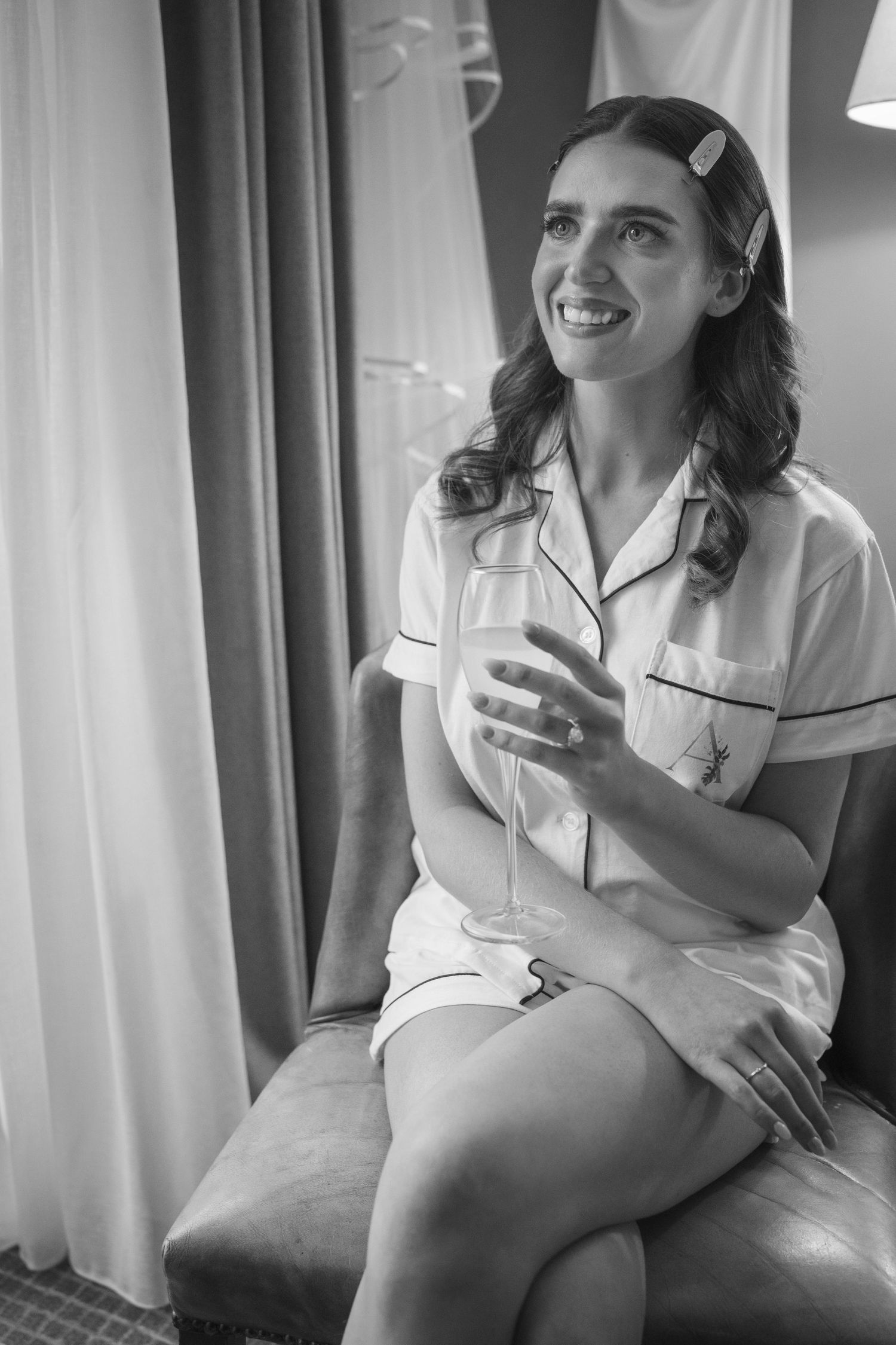Happy bride in personalized pajamas holding a champagne flute while sitting in a hotel room at the Manor House Mount Juliet wedding Kilkenny