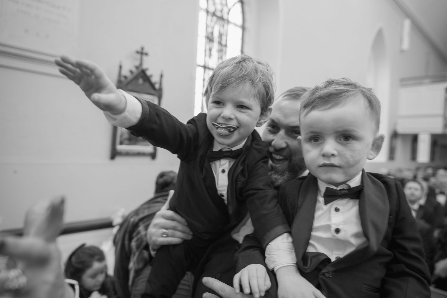 Black and white photo of two young boys in tuxedos at wedding ceremony, one pointing.