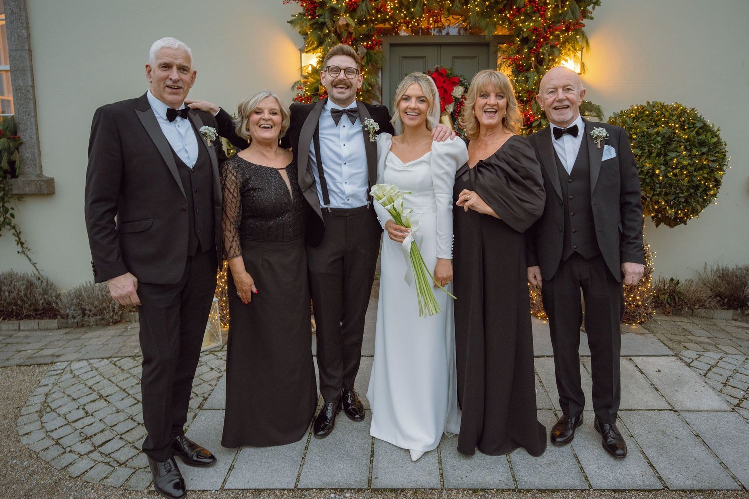 A wedding party of six poses outdoors in formal attire beside festive Christmas decorations.