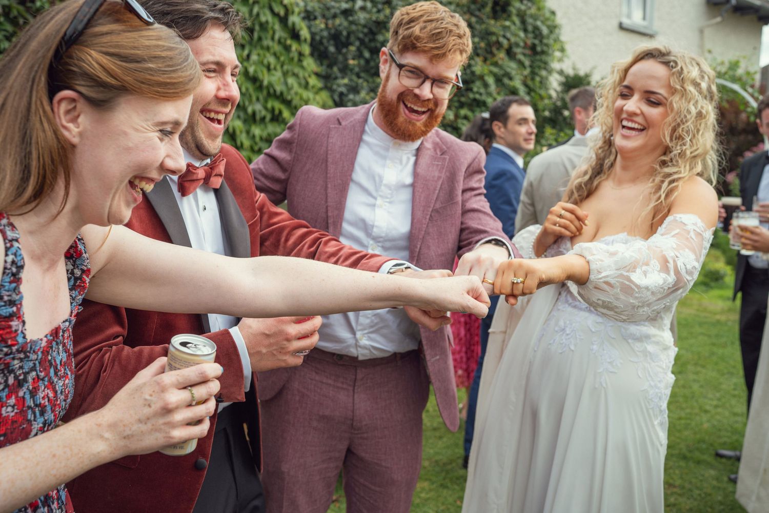 Laughing wedding guests reach toward bride in white off-shoulder gown at garden wedding reception in Co Meath.