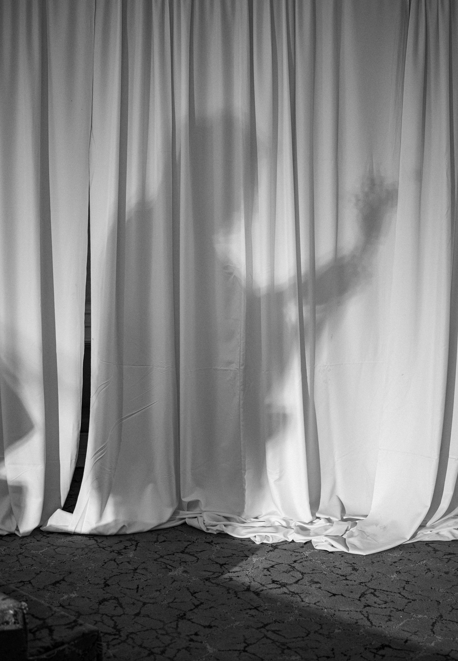Dramatic black and white silhouette of a person behind white curtain with hands raised.