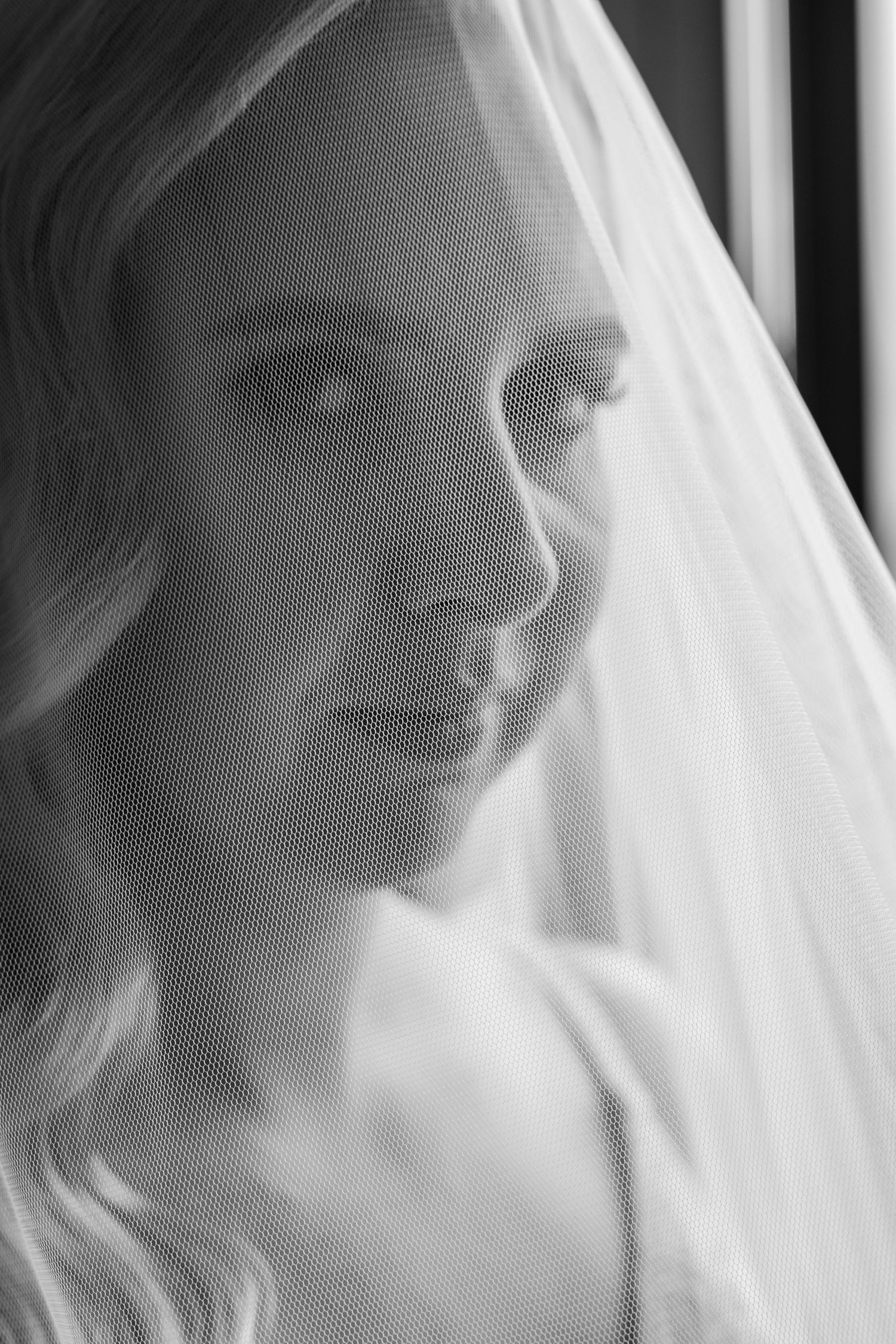 Black and white portrait of a bride wearing a delicate veil, gazing downward with soft elegant makeup.