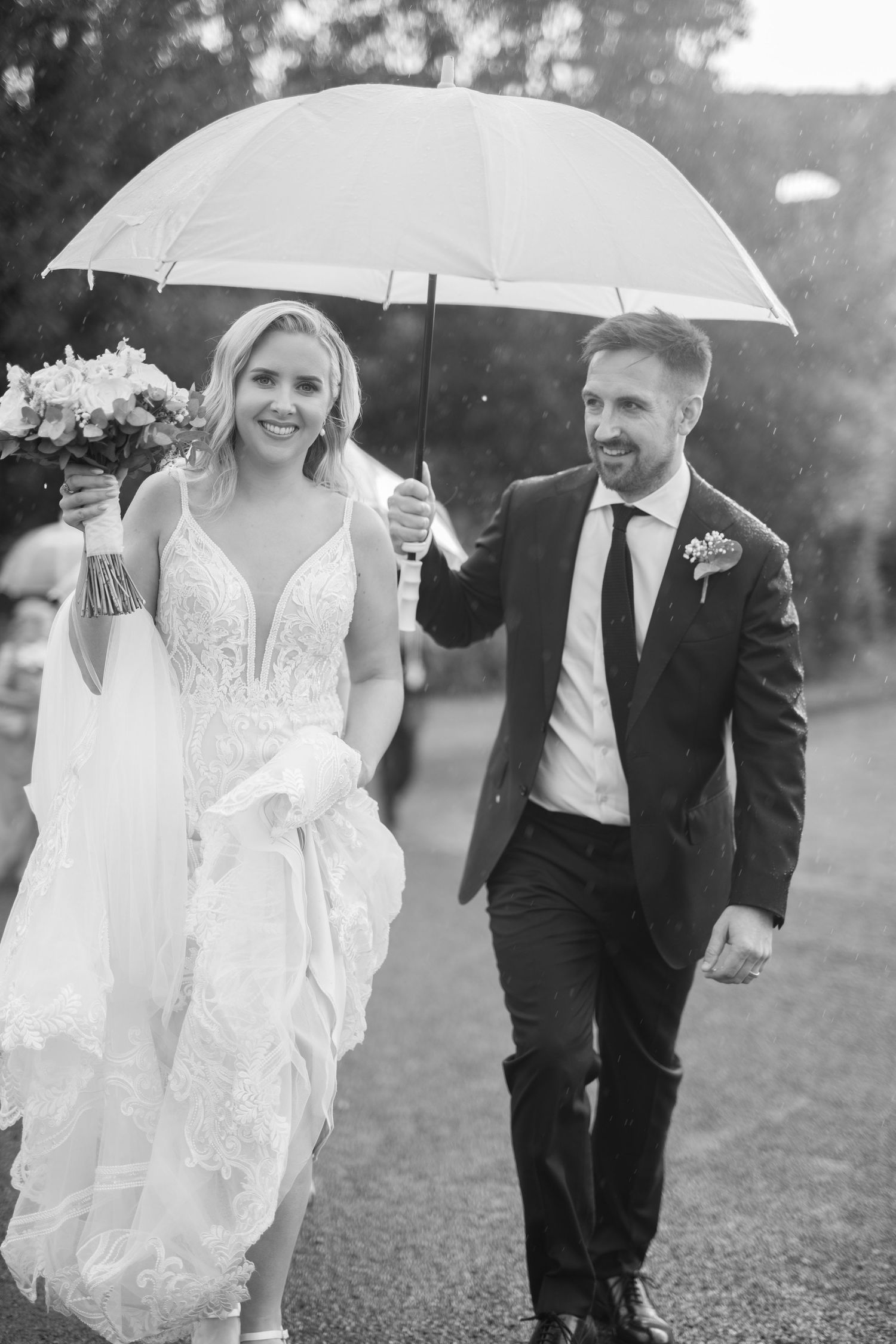 Smiling bride and groom walking together under umbrella in the rain at Trim Castle wedding in Co. Meath.