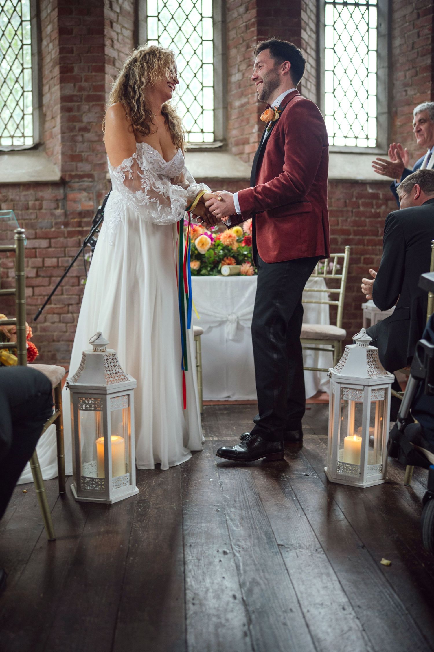 Bride and groom hold hands during wedding ceremony at red chapel Kells in Co Meath. surrounded by candlelit lanterns.
