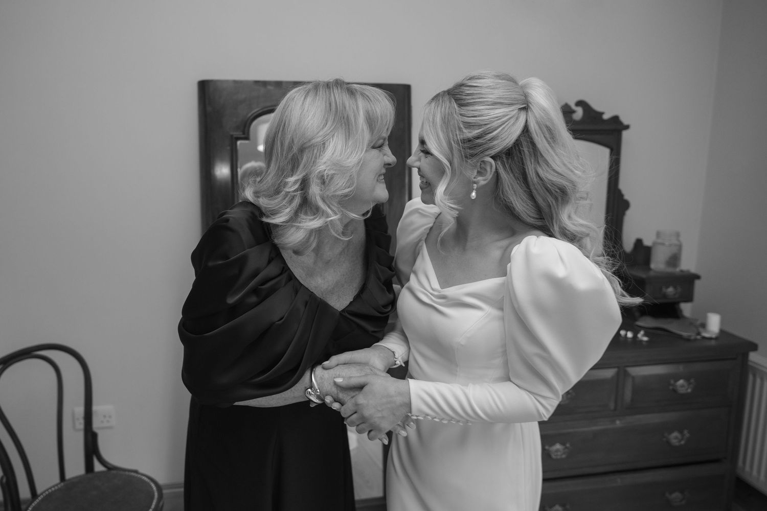 Black and white photo of an emotional bride sharing a tender moment with her mother before the wedding.