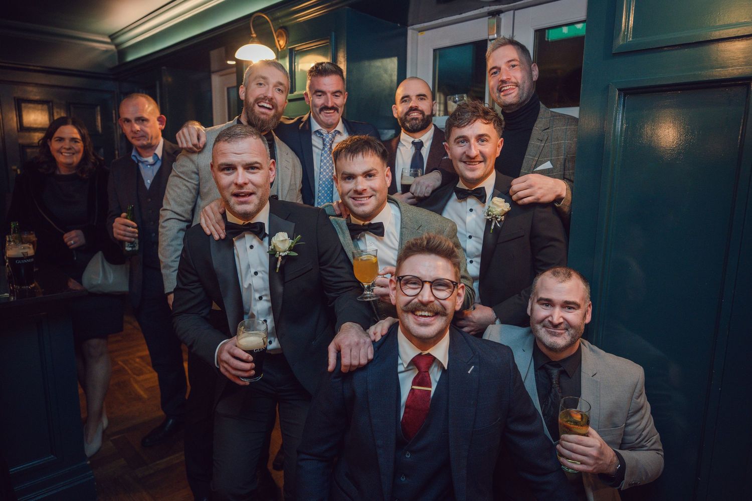 Large group wedding guests smiling and posing together in a stylish dark-paneled bar at Mount Juliet wedding in Kilkenny.