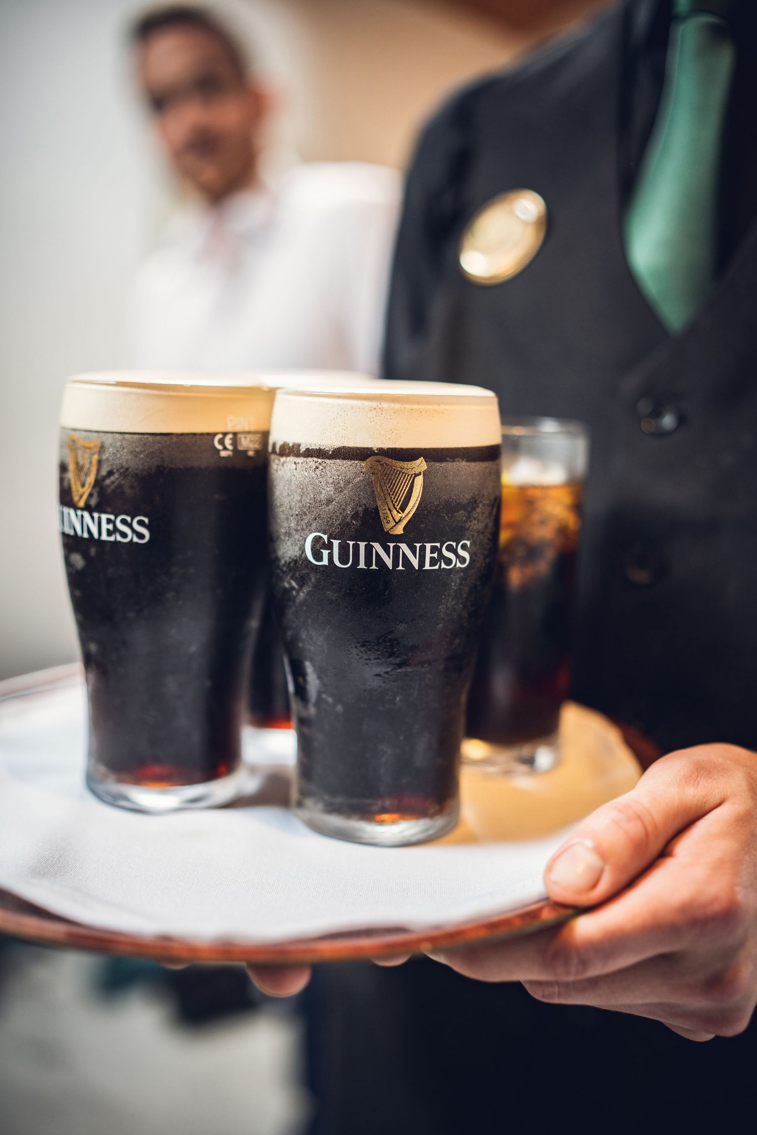 Waiter serving two pints of Guinness stout on a silver tray at a formal event.
