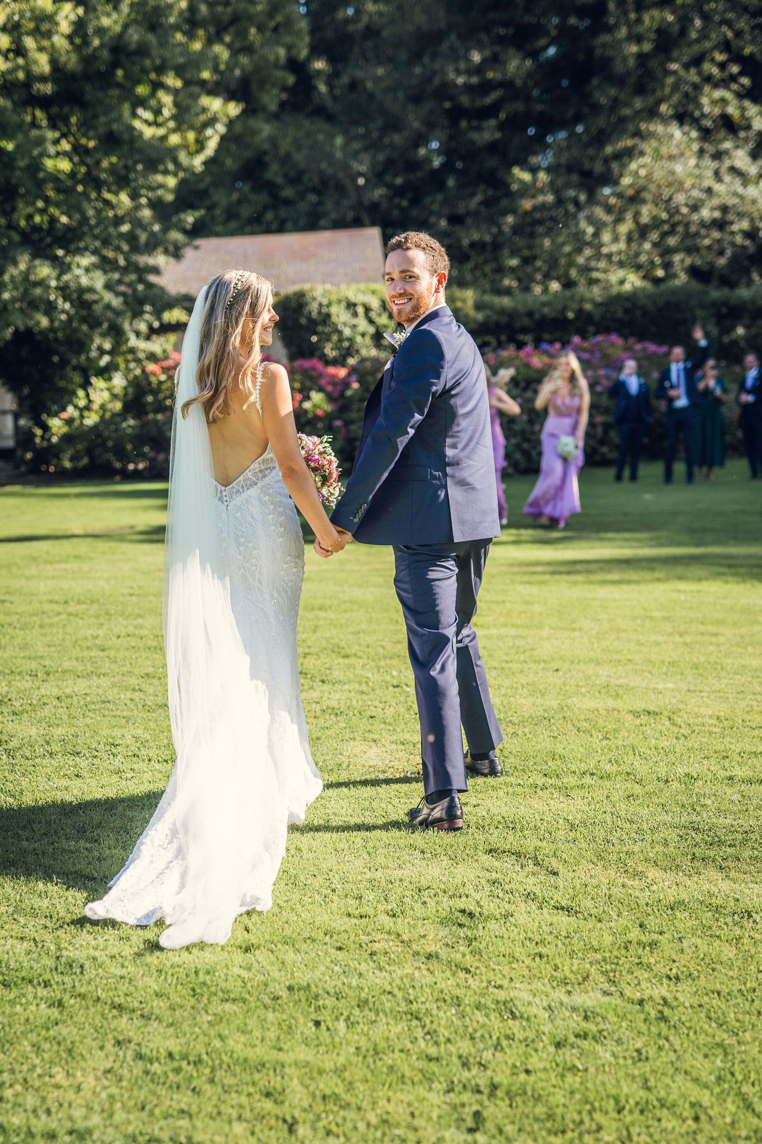 Bride and groom holding hands on green lawn at outdoor summer wedding.