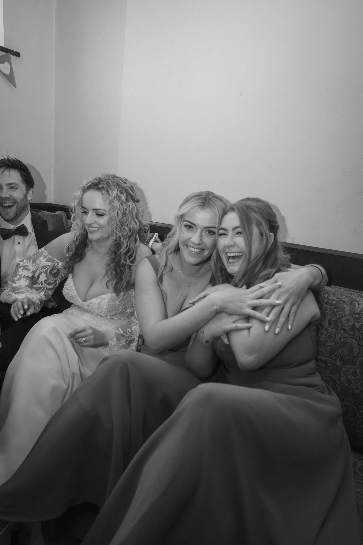 Candid photo of bride and two bridesmaids laughing and embracing joyfully on a sofa indoors outdoor garden wedding reception in Co Meath.