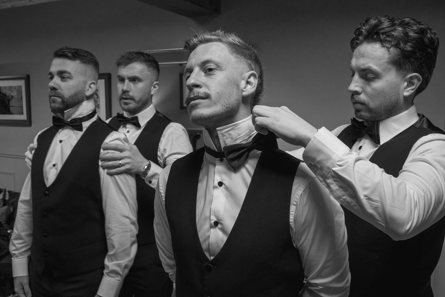 Groomsmen helping each other with bow ties in black and white photo.