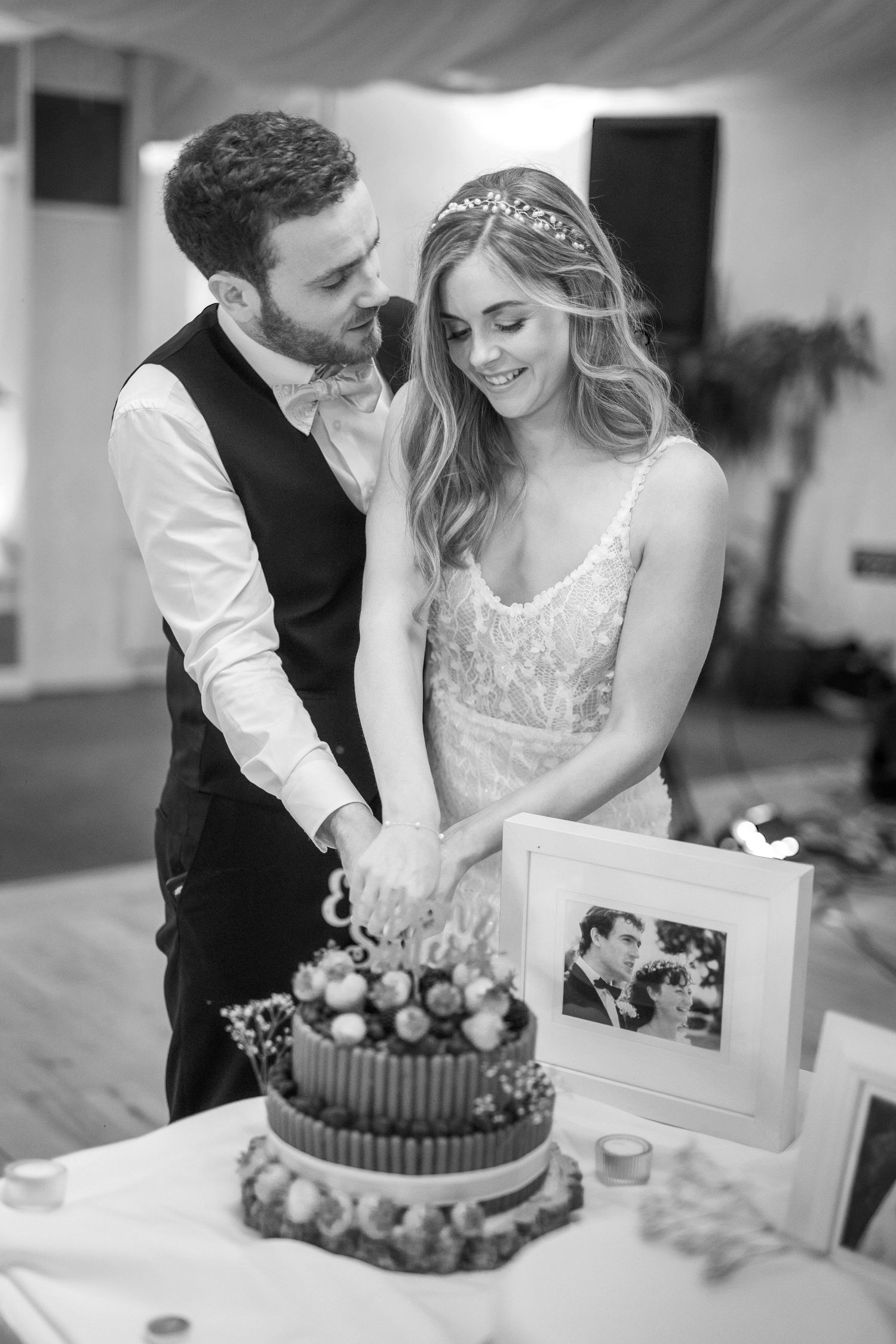 Bride and groom cutting their decorated wedding cake together in black and white, with framed photo displayed nearby.