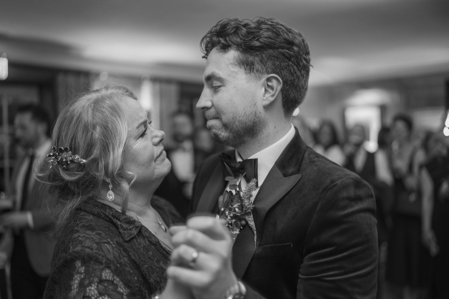 Groom shares emotional mother-son dance at wedding reception in black and white photo.