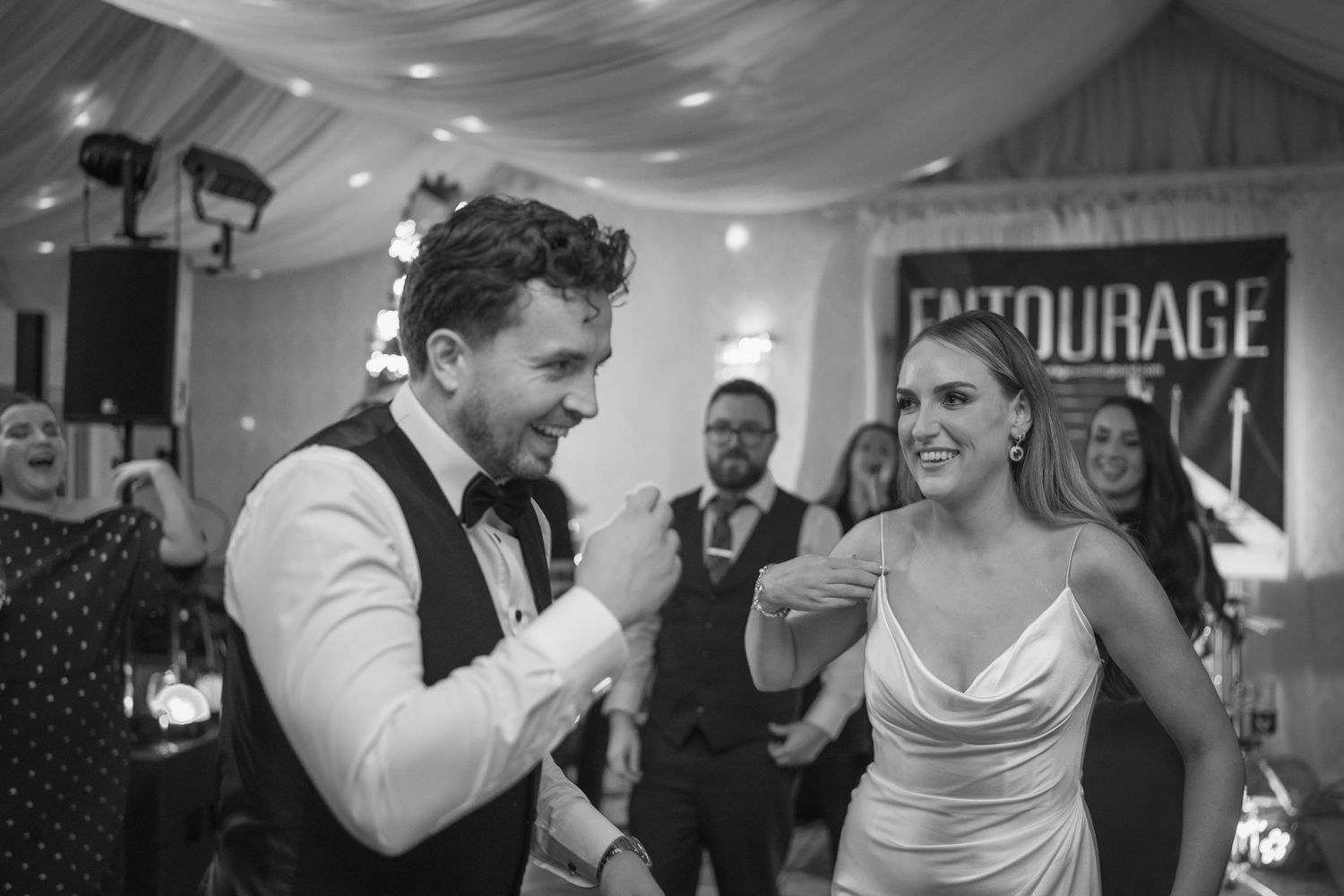 Bride and groom share joyful dance moment at wedding reception with band backdrop.