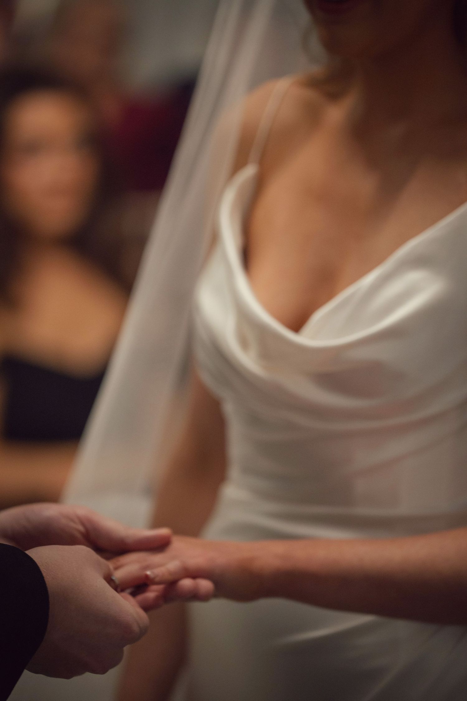 Close-up of ring exchange during wedding ceremony with bride in elegant satin gown.