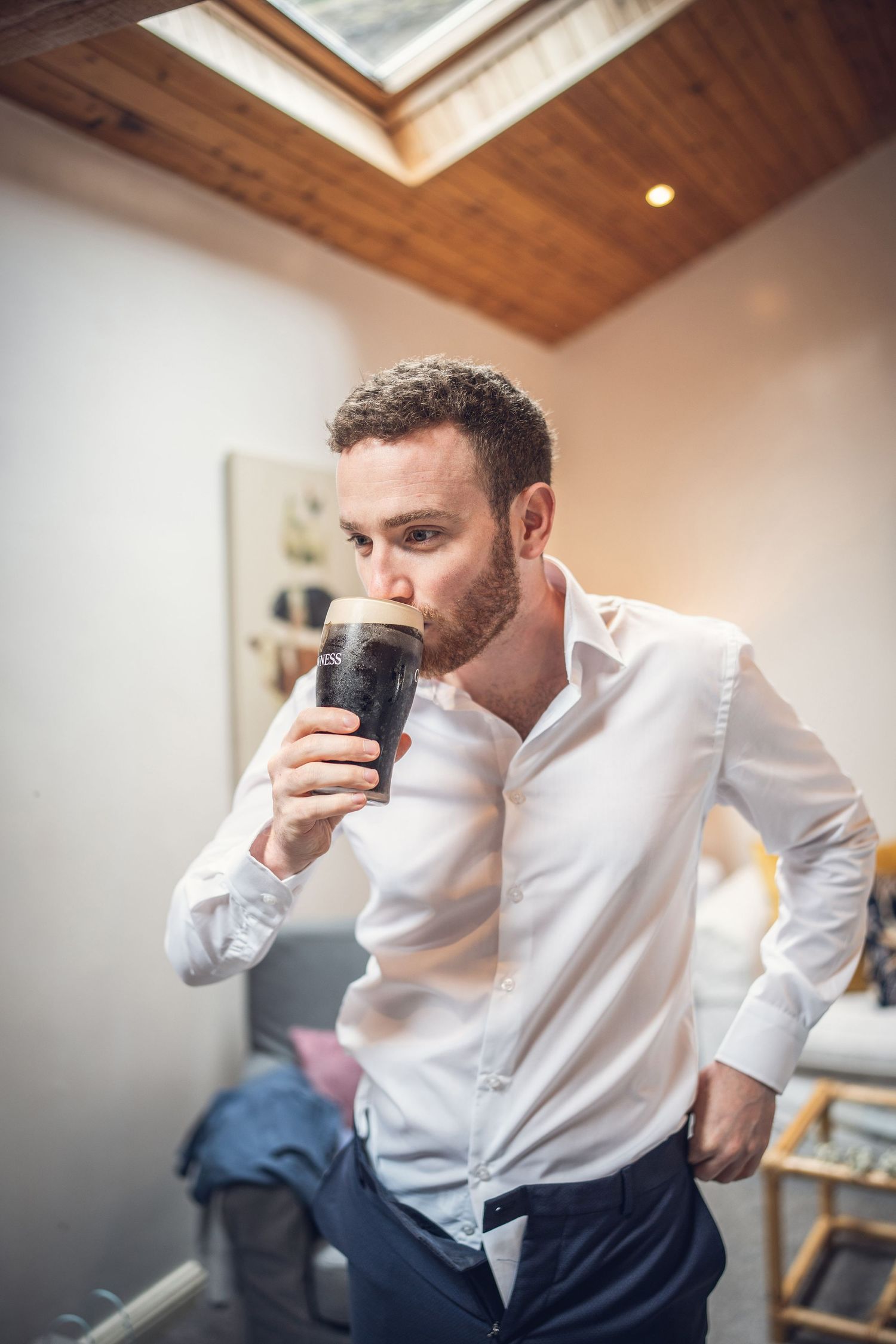 Groom in white shirt drinking a pint of Guinness while getting ready on wedding day.