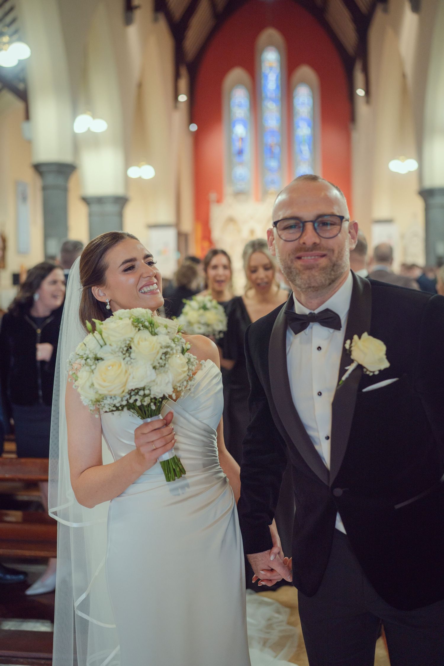 Joyful bride holding white rose bouquet with groom in black tuxedo after church wedding ceremony at Mount Juliet wedding Kilkenny.