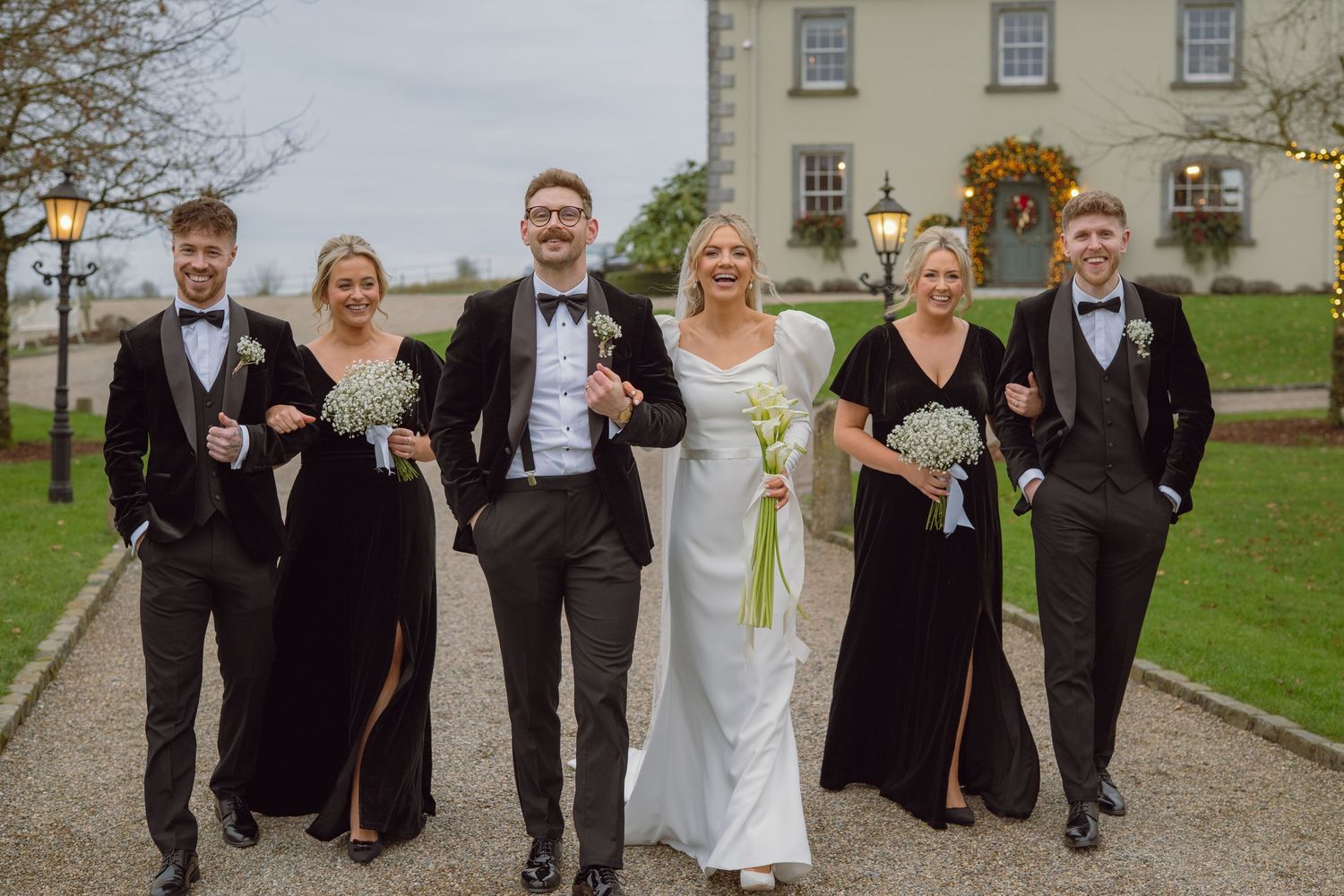 Wedding party walking in black and white attire outside an elegant country house venue.