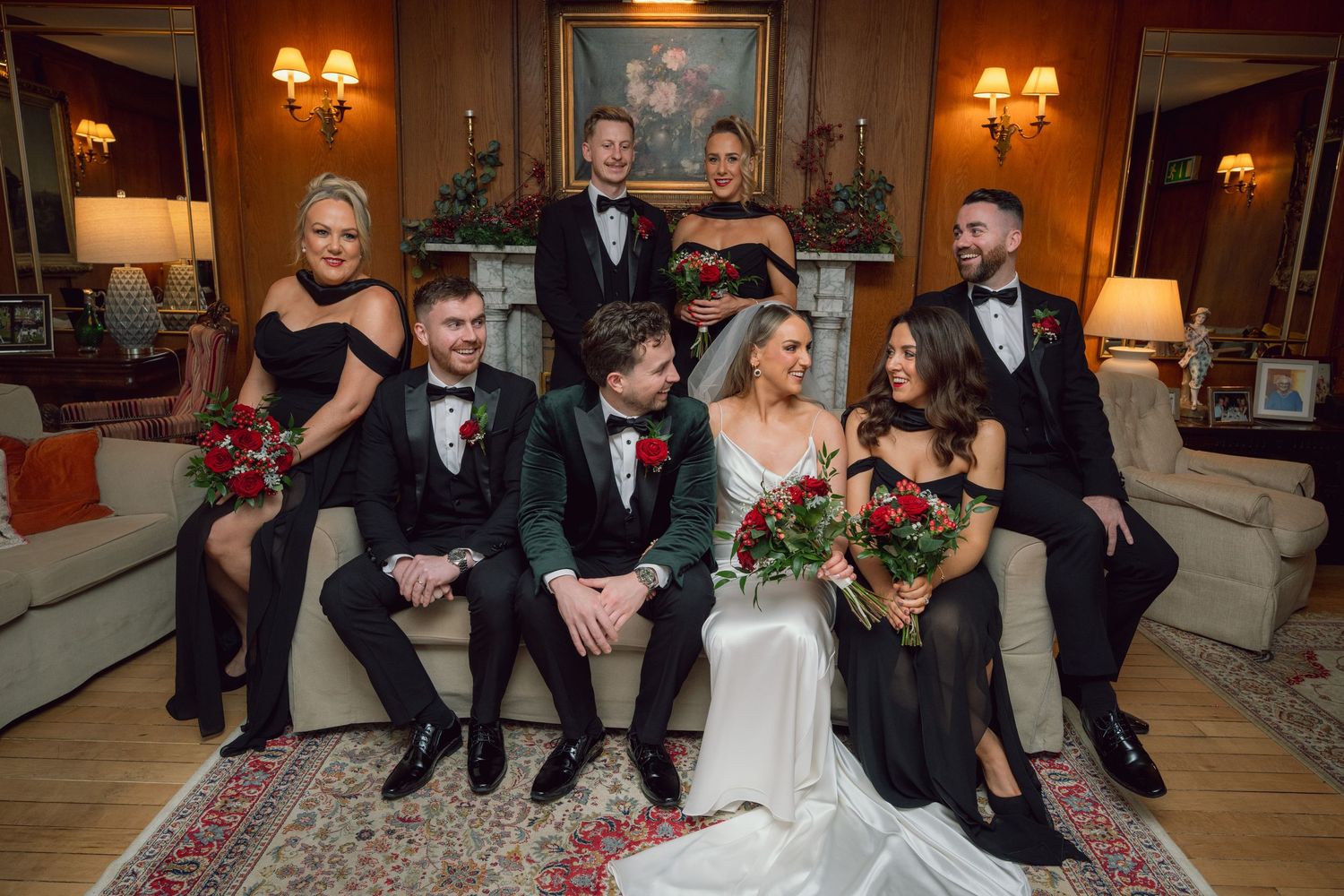 Wedding party posing together indoors with red roses and elegant decor.