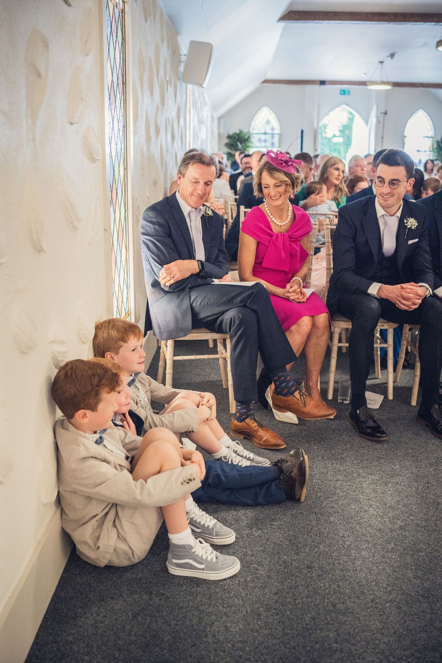 Wedding guests including two boys seated on floor during indoor ceremony.