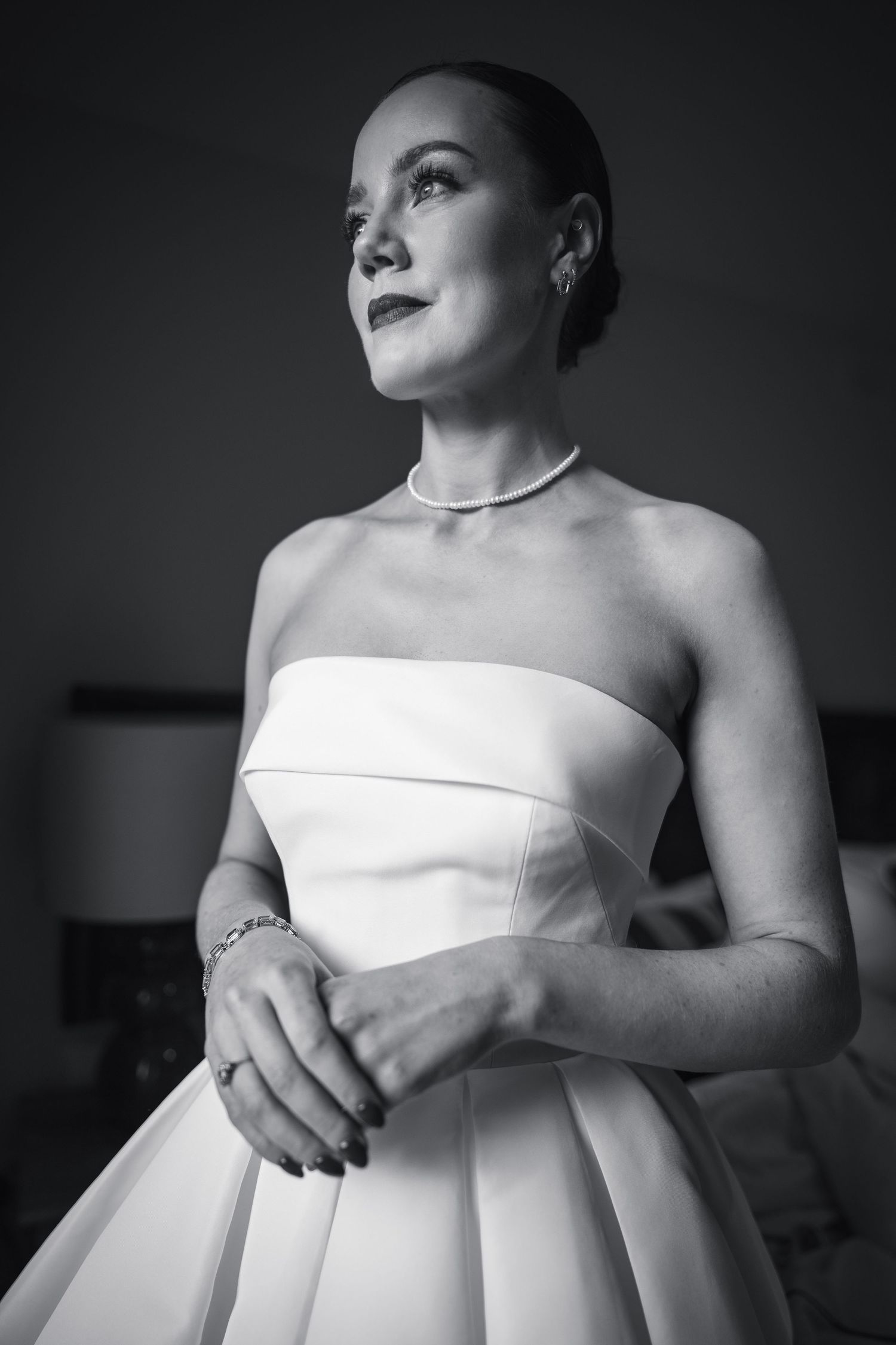 Elegant black and white portrait of bride in strapless white ball gown with pearl necklace and bracelet.