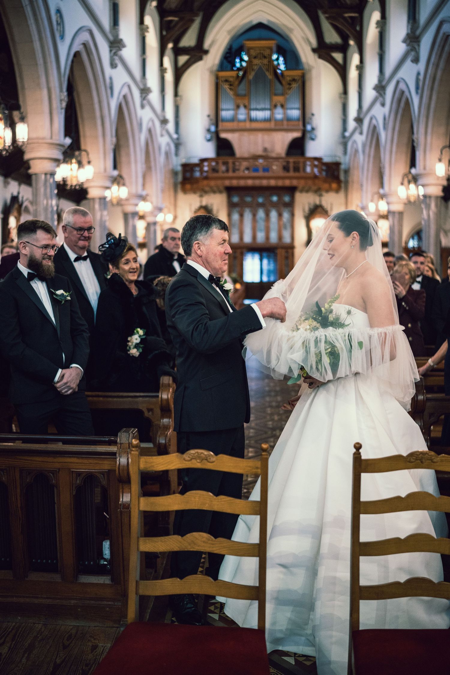 Father hands off bride in tulle ball gown and veil at church altar during wedding ceremony.